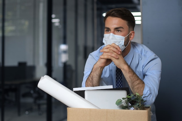 Dismissal employee in an epidemic coronavirus. Sad dismissed worker are taking his office supplies with him from office.