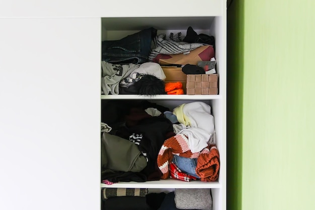 Photo disorder in wardrobe with colorful clothes. different clothes thrown on a white shelf