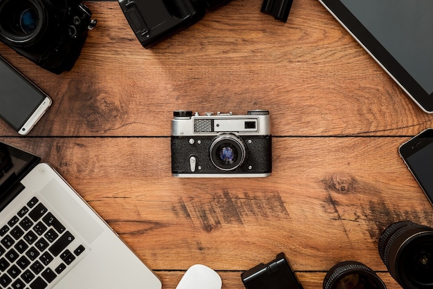 Displacement of old technology. Top view of retro camera surrounding by diverse equipment for photographer laying on the wooden grain