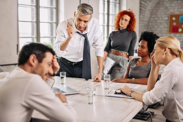 Displeased businessman arguing with colleagues on a meeting in the office and scolding one of them