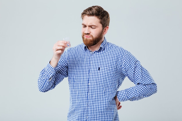 Displeased frowning bearded young man with bottle of pills over white wall