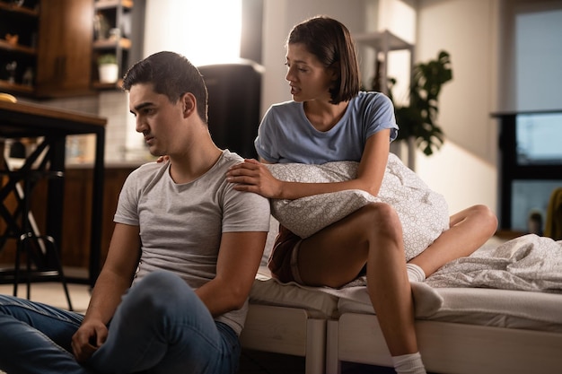 Displeased man ignoring his girlfriend while she is trying to talk with him after the argument in the bedroom