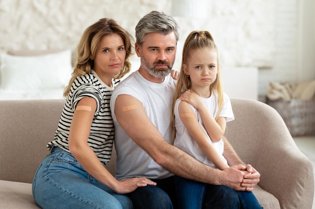 Displeased vaccinated family showing arms with adhesive bandage at home