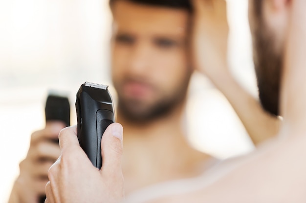 Displeased with his new shaver. Rear view of frustrated young man holding electric shaver and expressing negativity while standing in front of the mirror