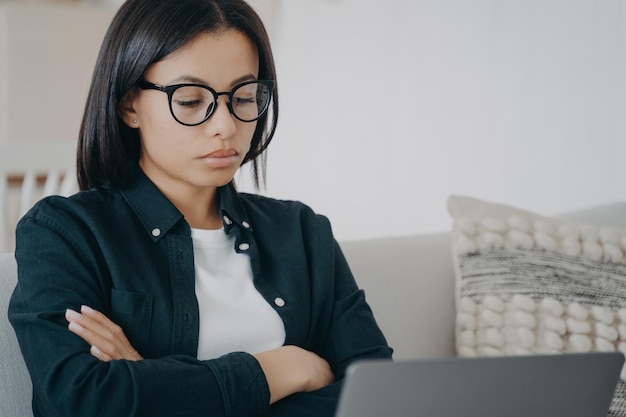 Displeased woman in glasses is looking seriously at laptop screen Businesswoman examining report