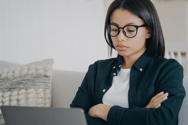 Displeased woman in glasses is looking seriously at laptop screen Businesswoman examining report