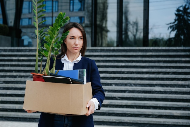 A displeased woman holding a cardboard box embodies the frustration and discontentment resulting from dismissal and job loss Struggles of a Troubled Employee Woman Holding Cardboard