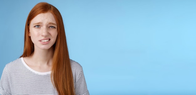 Photo displeased young awkward redhead girl cringe full disbelief smirking frowning confused look questioned doubtful hearing nuisance dumb story standing blue background uncertain