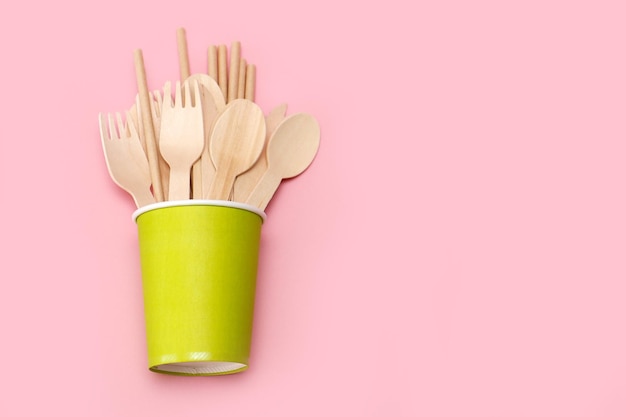 disposable bamboo cutlery in paper green glass on pink background with copy space