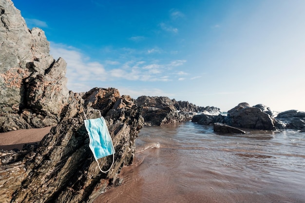 Disposable face mask on the rock of the beach thrown away polluting the ocean and the planet