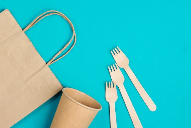 Disposable kitchenware of natural materials. Eco friendly concept. Wooden forks, empty craft coffee cup, bag on blue background. Top view