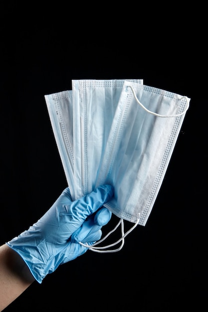 Disposable medical sanitary surgical medical masks in hand in blue glove isolated on black