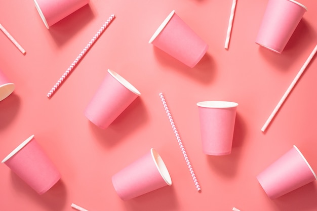 Disposable paper cups and drinking straws on pink background.