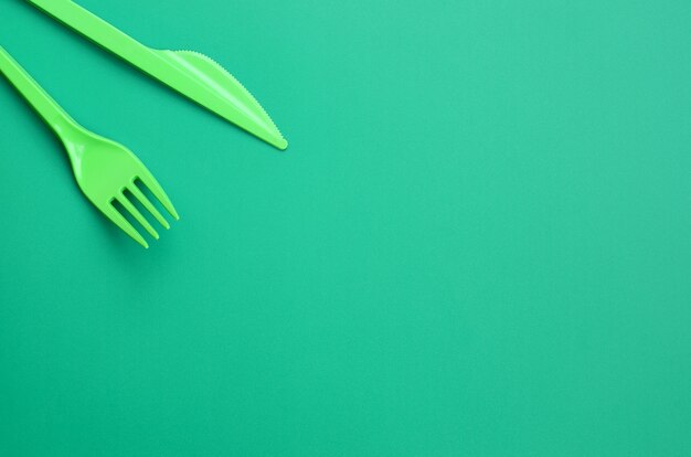 Disposable plastic cutlery green. Plastic fork and knife lie on a green background surface