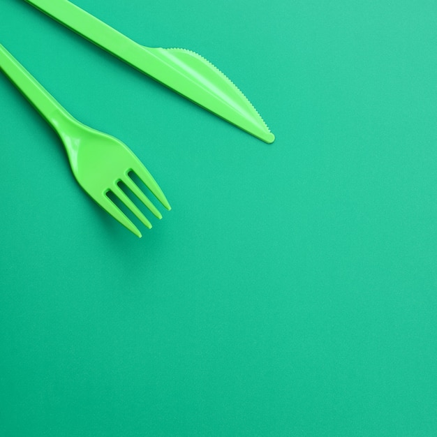 Disposable plastic cutlery green. Plastic fork and knife lie on a green background surface