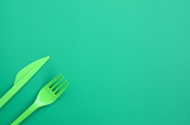 Disposable plastic cutlery green. Plastic fork and knife lie on a green background surface