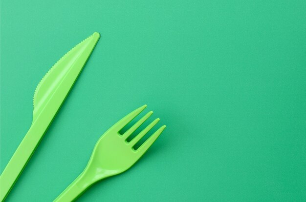 Disposable plastic cutlery green. Plastic fork and knife lie on a green background surface