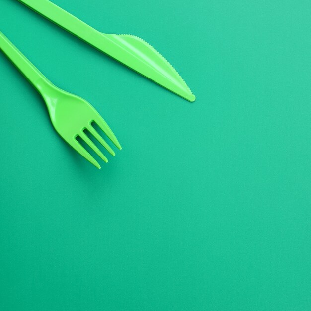 Disposable plastic cutlery green. Plastic fork and knife lie on a green background surface