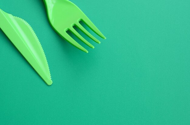 Disposable plastic cutlery green. Plastic fork and knife lie on a green background surface