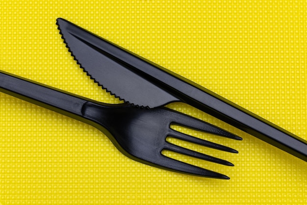 Disposable plastic tableware. Fork and knife on a yellow background.