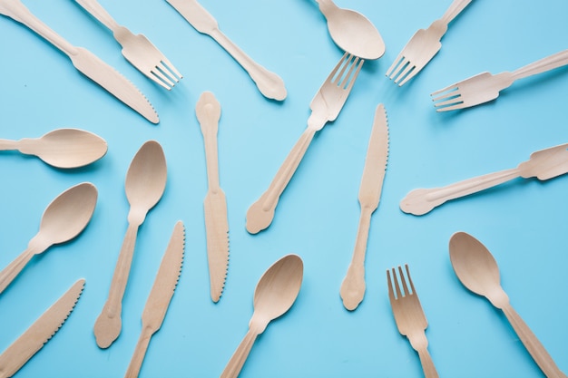 Disposable tableware from natural wooden materials, spoon, knife, and fork, eco-friendly for picnic on blue. Top view.