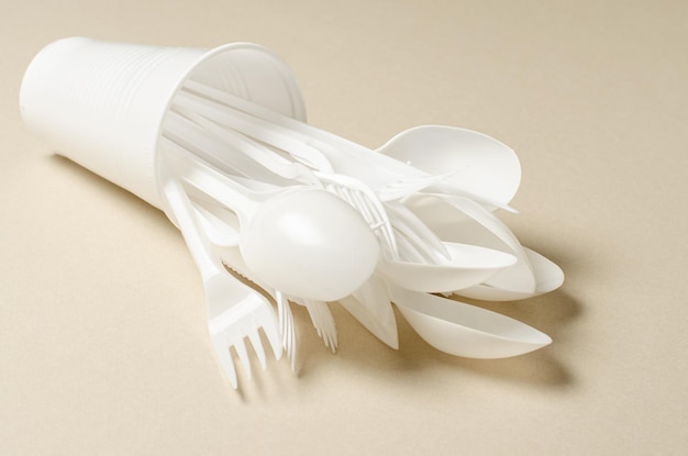 Disposable white plastic tableware on a beige background The concept of nature pollution Copy space