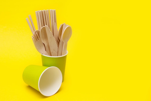 disposable wooden spoons forks and knives in a green paper cup on a yellow background with copyspace recycled