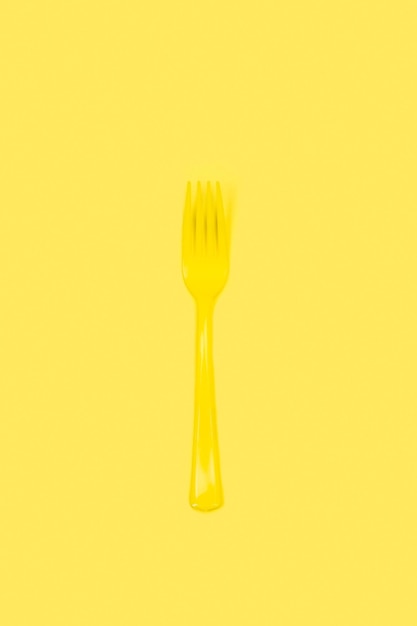 Disposable yellow plastic fork on a yellow background with copy space