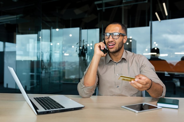 Dissatisfied businessman in the office with a bank credit card calls customer support blocked card