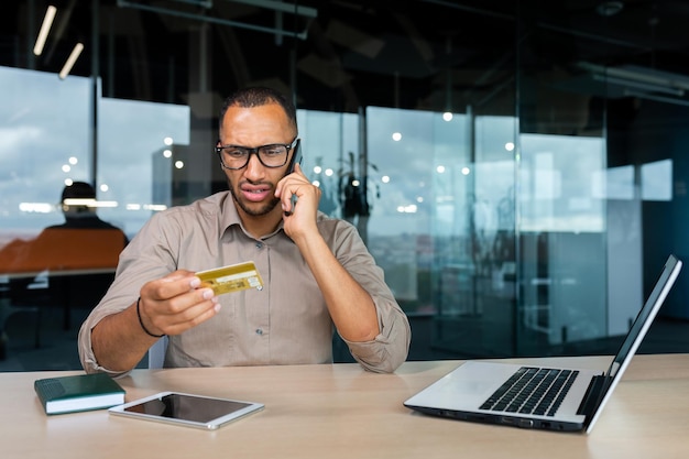 Dissatisfied businessman in the office with a bank credit card calls customer support blocked card