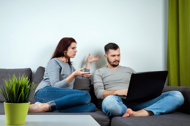 Dissatisfied girl looks at a guy playing on a laptop