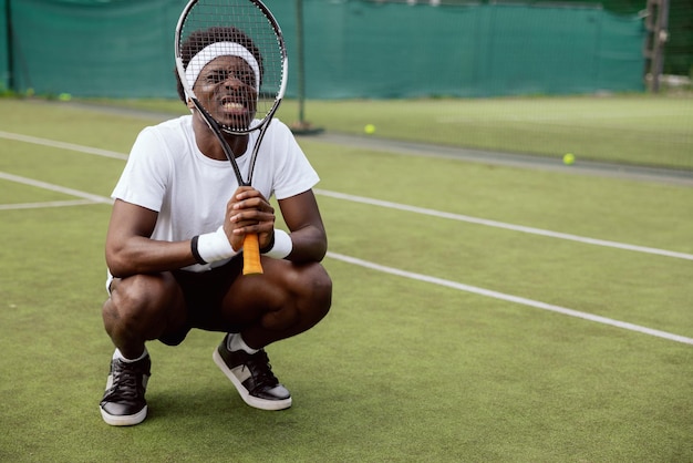 Dissatisfied with serve while playing tennis young africanlooking guy squatted on grass