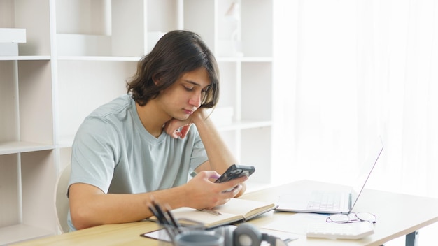 Distance education concept Teen boy using phone to check class schedule of online learning at home