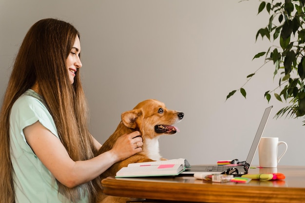 Distance education Girl student with laptop study online with her lovely Corgi dog at home Young woman hug Welsh Corgi Pembroke and making notes in notebook Lifestyle with domestic pet