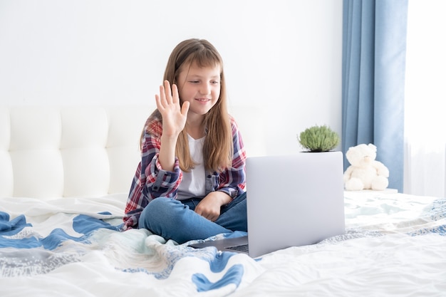 Distance learning online education. Schoolgirl studying with digital laptop notebook and doing school homework lying on bed at home