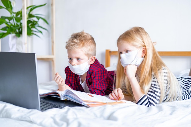 Distance learning online education Sickness school boy and girl in medical mask studying at home with digital tablet laptop notebook and doing homework Sitting on bed with training books