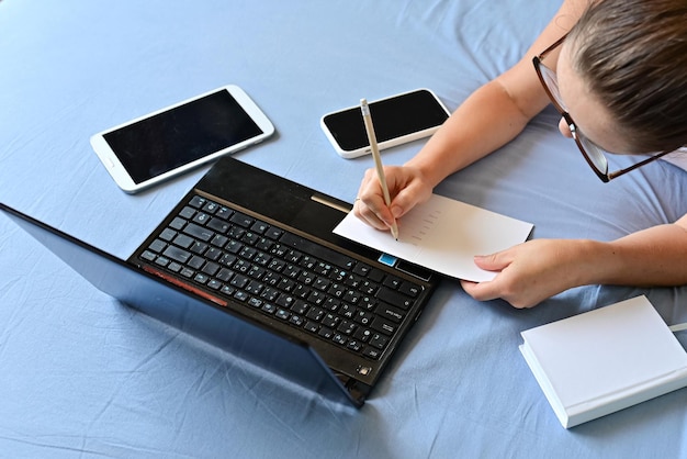 Distance learning online education and work Cropped woman girl working office work remotely from home on bed Using computer and drinking coffee