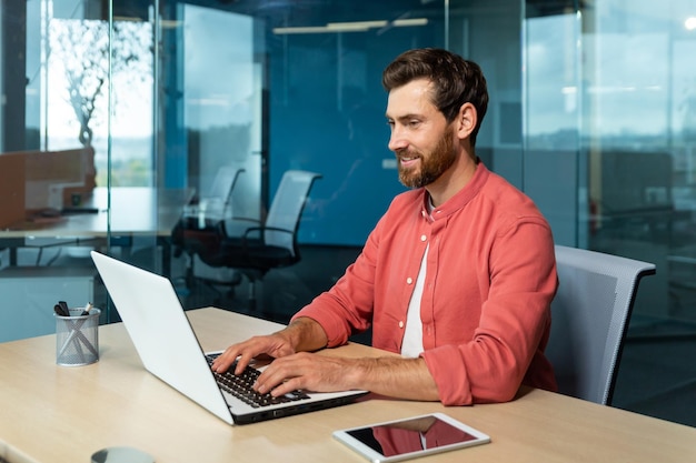 Distance learning portrait of a young male student in a red shirt sitting at the desk in the office