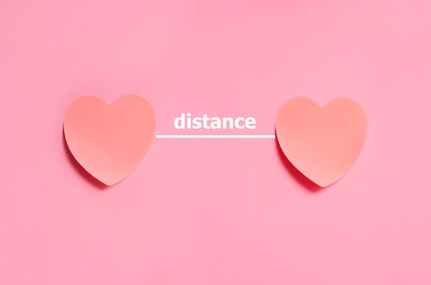 Distance text placed between two hearts made from paper on the pink background