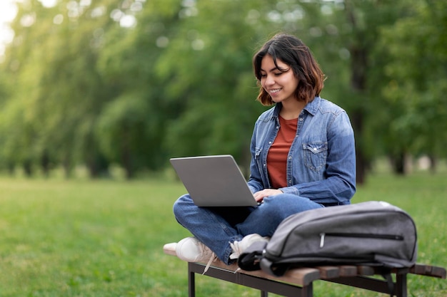 Distant Learning Arab Female Student Using Laptop While Sitting On Bench Outdoors