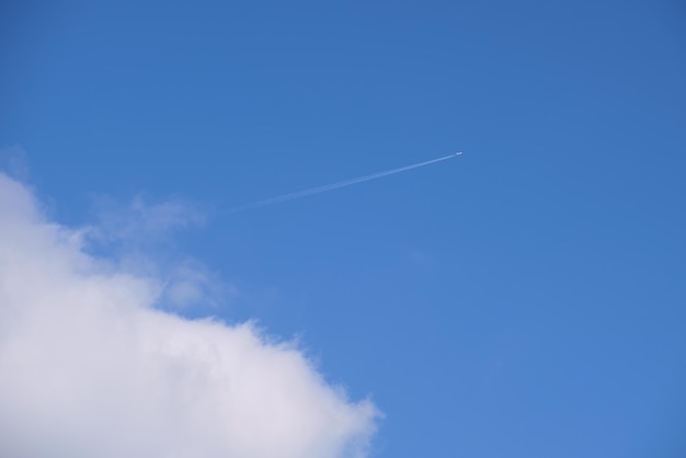 Distant passenger jet plane flying on high altitude on blue sky with white clouds leaving smoke trace of contrail behind. Air traveling concept.