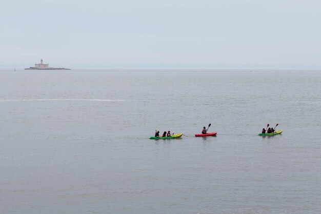 Distant view of people canoeing on sea against sky