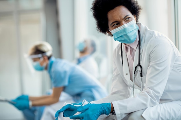 Distraught African American female doctor with protective face mask at hospital hallway