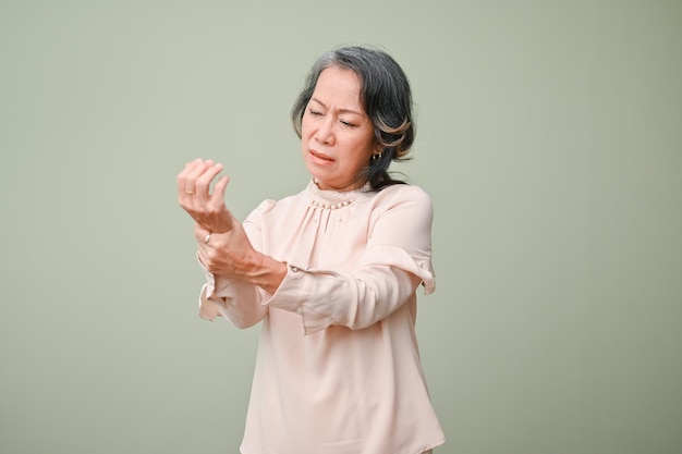 Distressed elderly Asian woman holding her wrist massaging her aching wrist isolated background