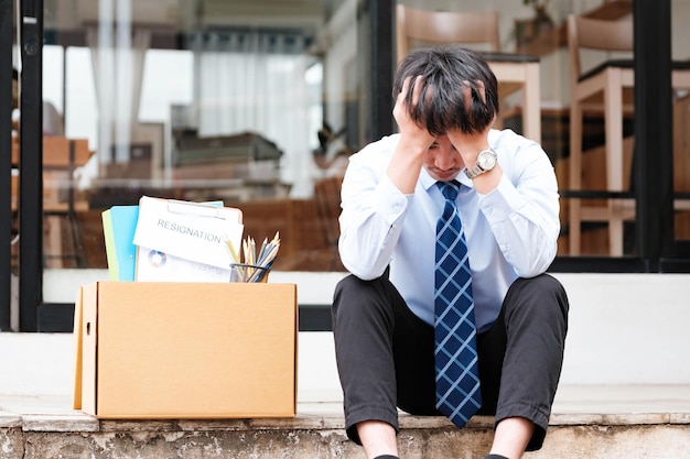 Photo distressed man sits outside office with his belongings postresignation