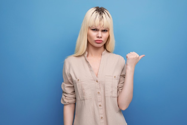 Distressed sad blond young woman shows her hand towards the wall