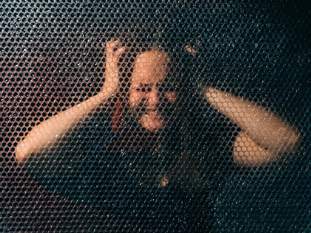 Disturbed woman. Migraine attack. Anxiety problem. Textured art portrait of stressed out lady in black suffering from pain touching head in darkness behind plastic bubble wrap.