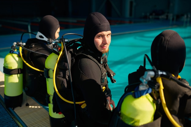 Divemaster and two divers in scuba gear preparing for the dive, diving school. Teaching people to swim underwater, indoor swimming pool interior on background