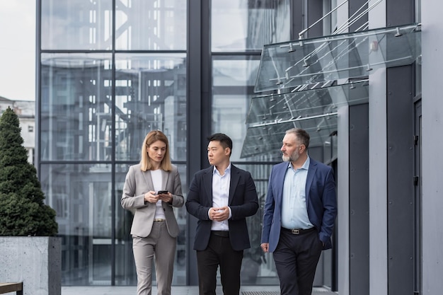 Diverse business group three male and female workers walking and chatting discussing plans outside