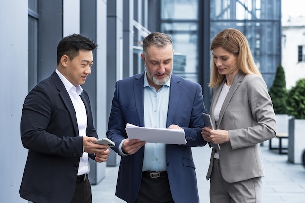 Diverse business team three colleagues employees discuss documents contract outside office building